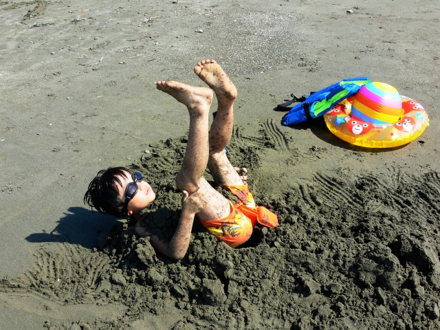 砂浜にひっくり返って遊ぶ水着姿の少年